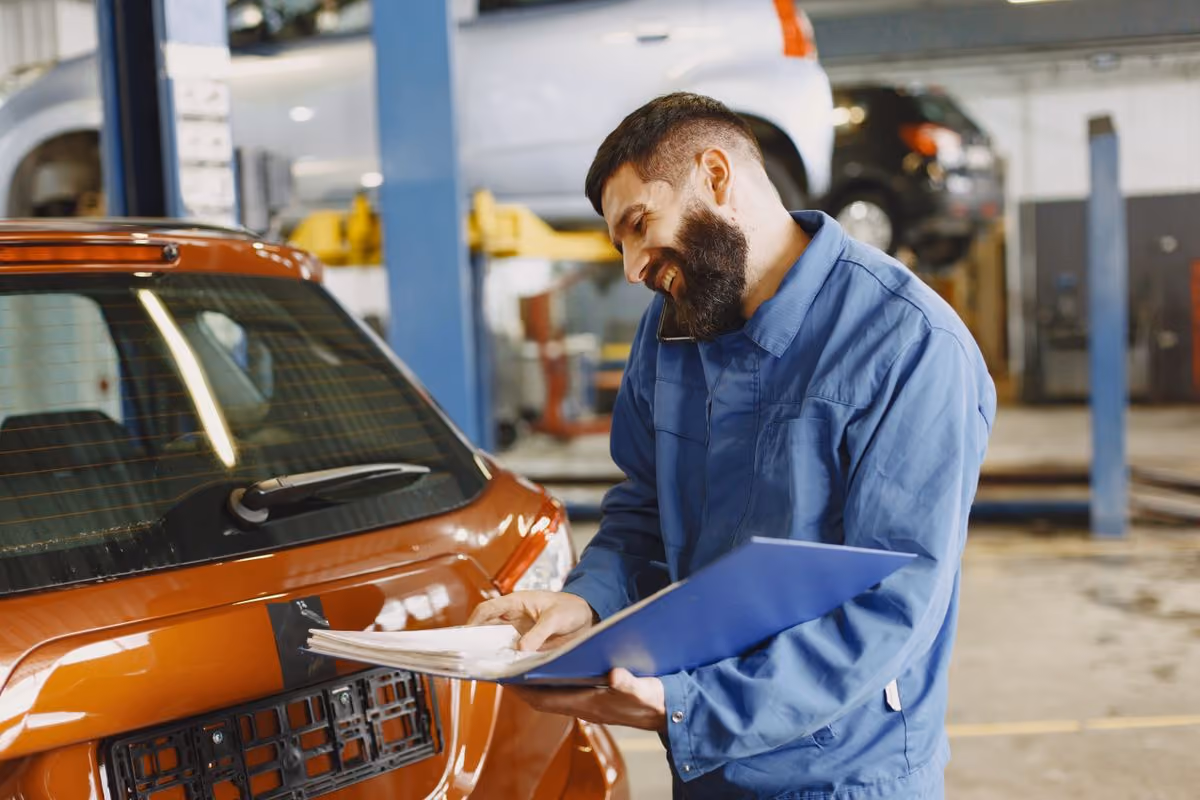 A technician in coveralls walking an inspection around a vehicle in a service bay